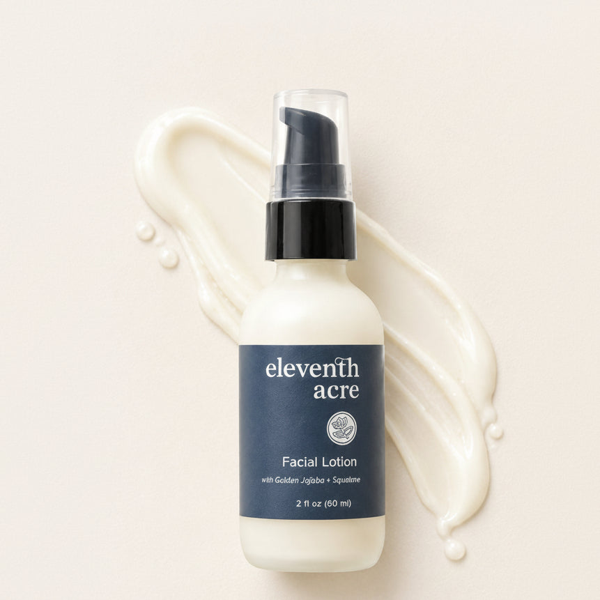 Eleventh Acre Facial Lotion in a frosted white bottle with a navy blue label and black pump, styled on a cream background with a cream lotion smear behind it.