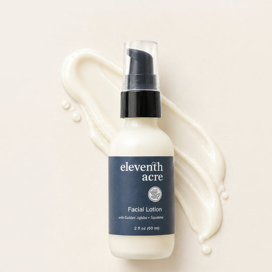 Eleventh Acre Facial Lotion in a frosted white bottle with a navy blue label and black pump, styled on a cream background with a cream lotion smear behind it.
